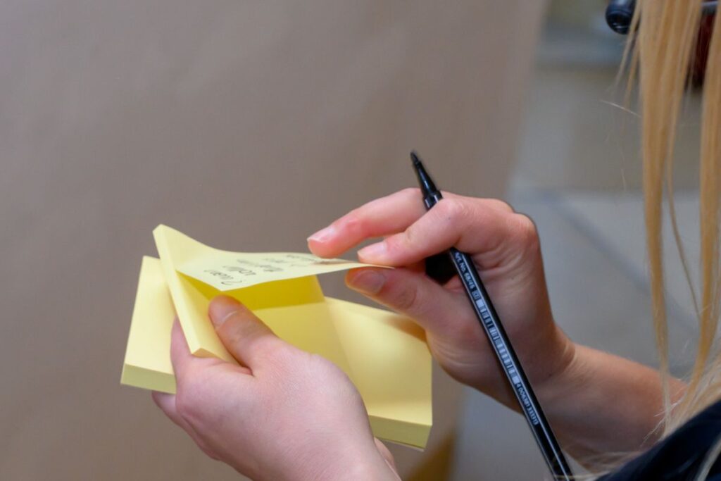 Teammitglied erfasst Ideen und Maßnahmen für die Weiterentwicklung der Organisation. Das Bild veranschaulicht agile Transformation, die Begleitung von Veränderungsprozessen, die Einführung agiler Arbeitsweisen, kontinuierliches Lernen sowie die Entwicklung einer Unternehmenskultur, die Anpassungsfähigkeit, Zusammenarbeit und Innovation fördert.